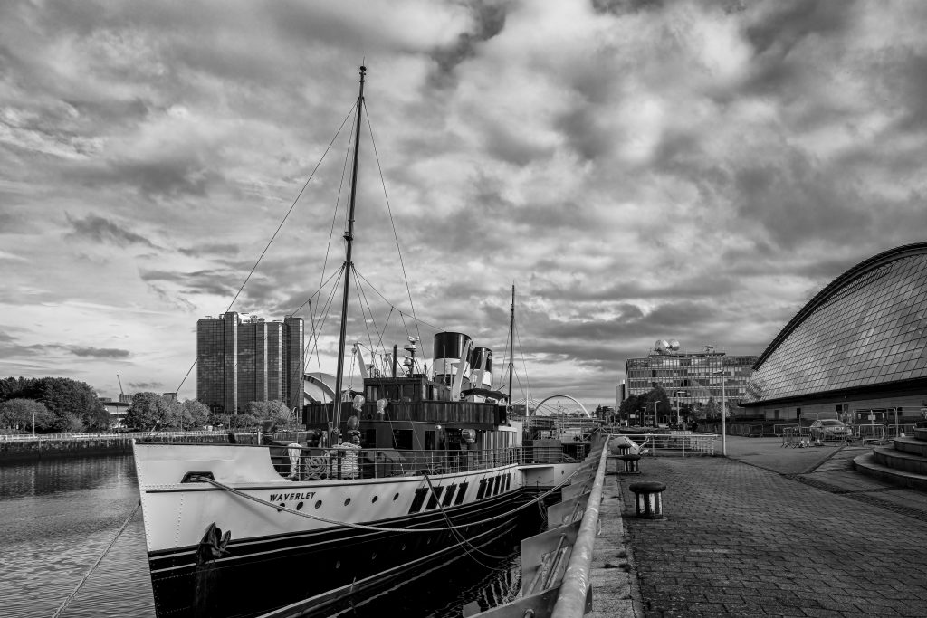 A black and white photograph with a ship on water and clouds filling the sky.