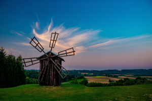 A windmill in the countryside with green fields and a blue and pale pink sky.